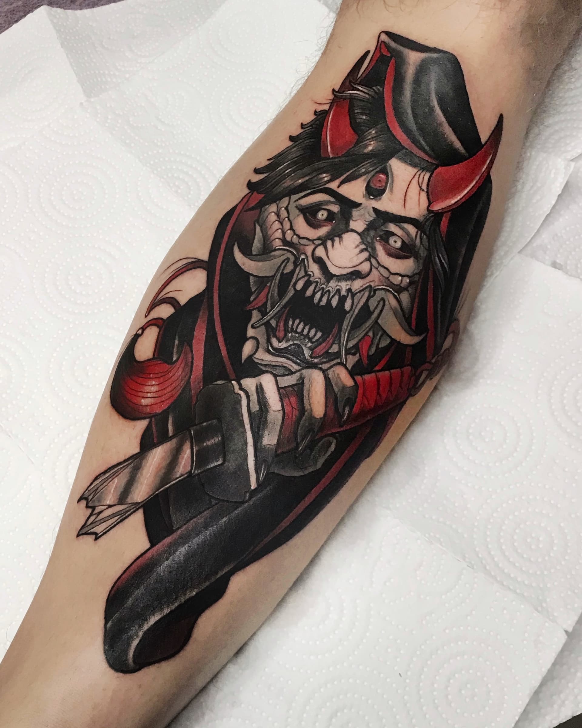 Neo traditional tattoo of a horned demon figure with red accents holding a broken katana — bold Japanese-inspired design