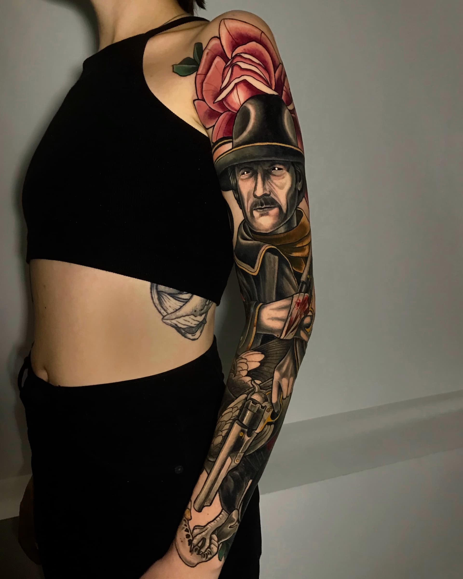 Neo traditional sleeve tattoo of a man in a hat with a revolver and large red rose — bold illustrative design