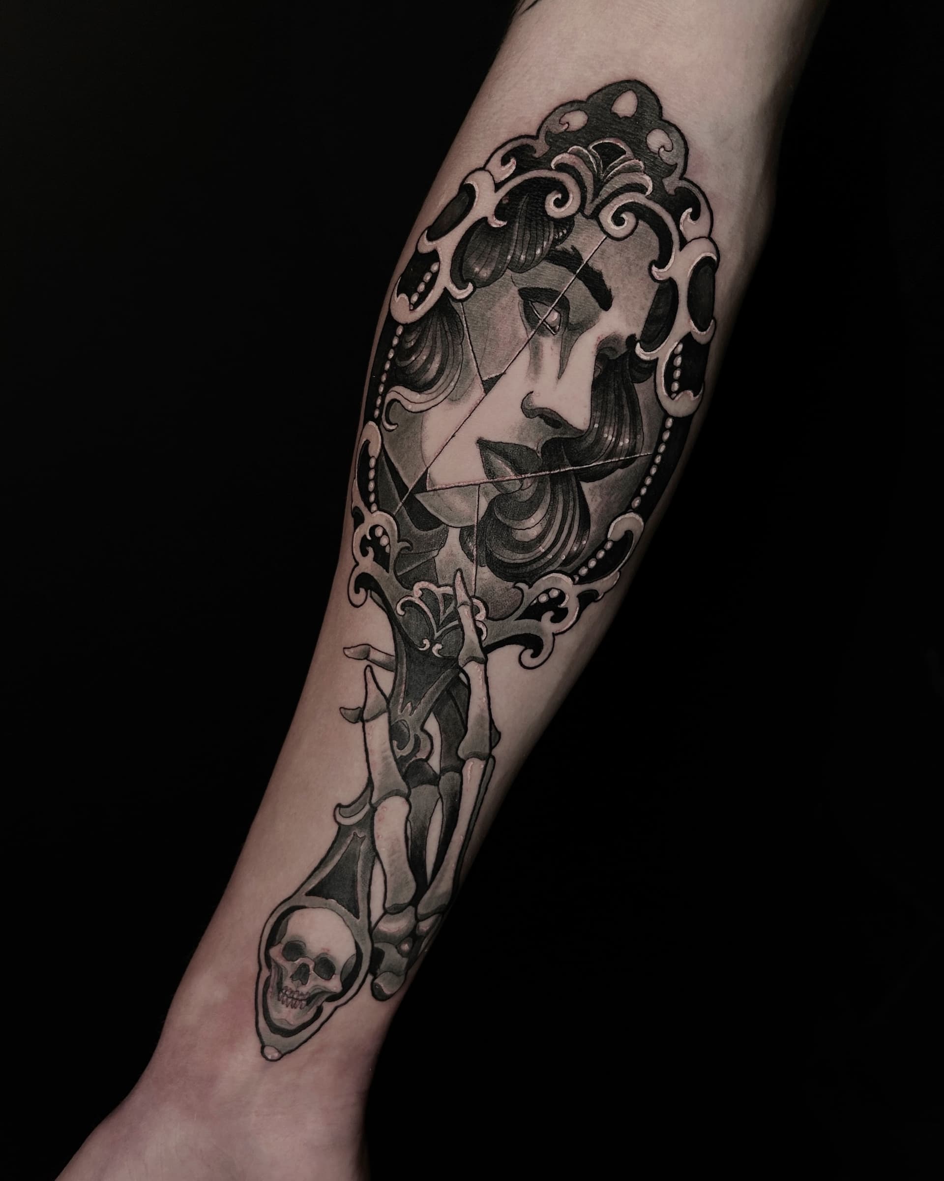 Neo traditional black and grey tattoo of a woman's face in a broken ornate mirror with a skeletal hand — detailed illustrative design