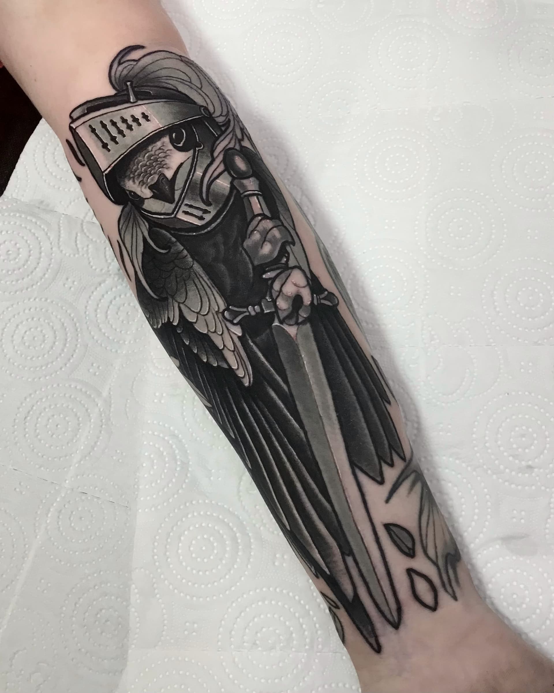 Black and grey forearm tattoo of a bird knight in armor holding a sword — detailed illustrative piece